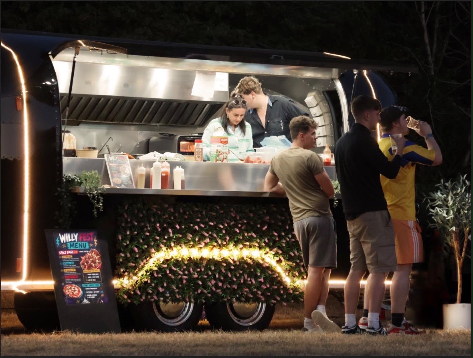 The Airstream kitchen lit up and serving a crowd after dark.