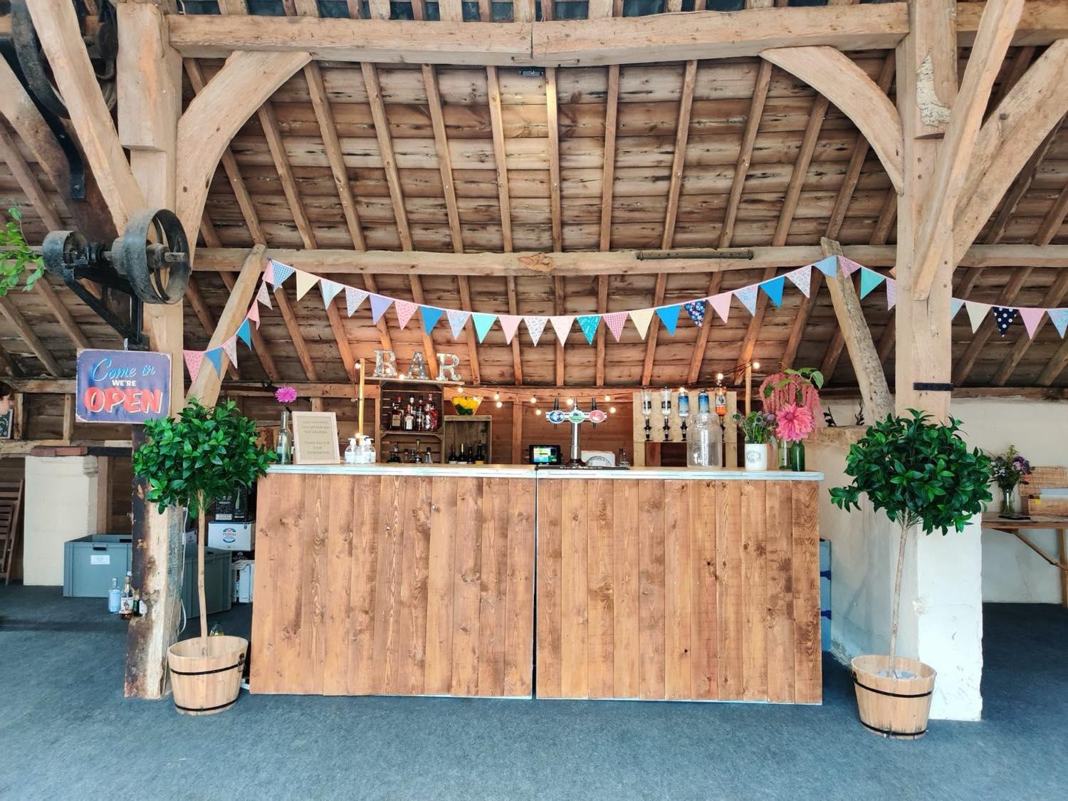 A rustic wooden bar with taps and spirits inside a timber-framed barn with bunting.