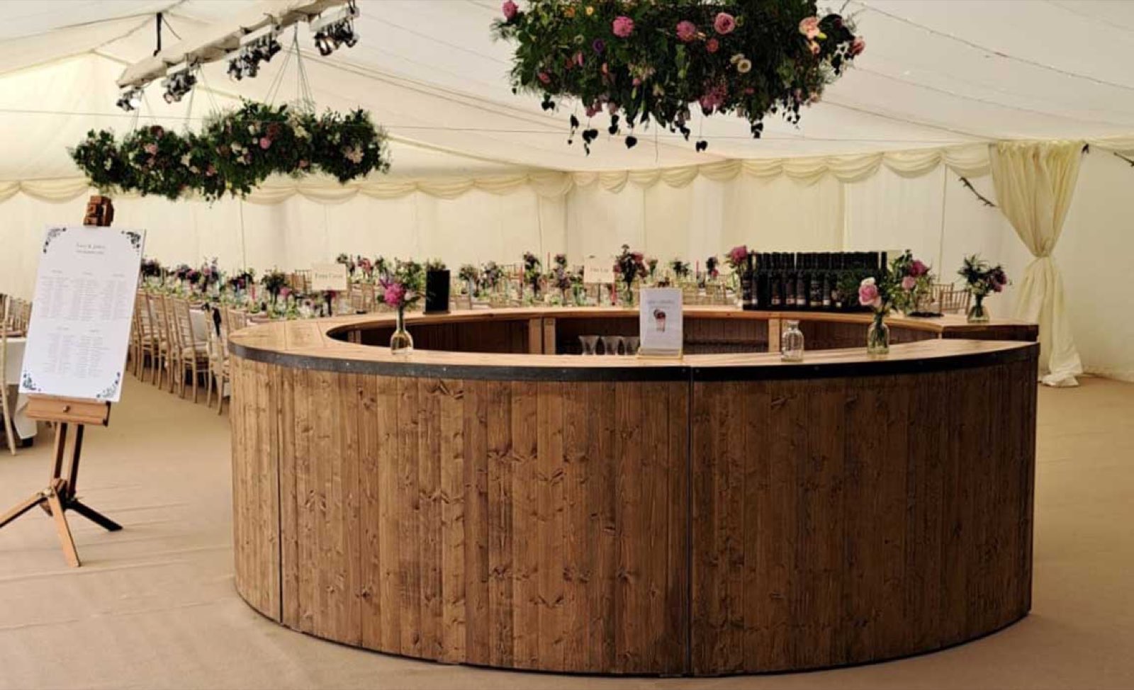 A full round rustic bar set up inside a wedding marquee, hanging flowers above.