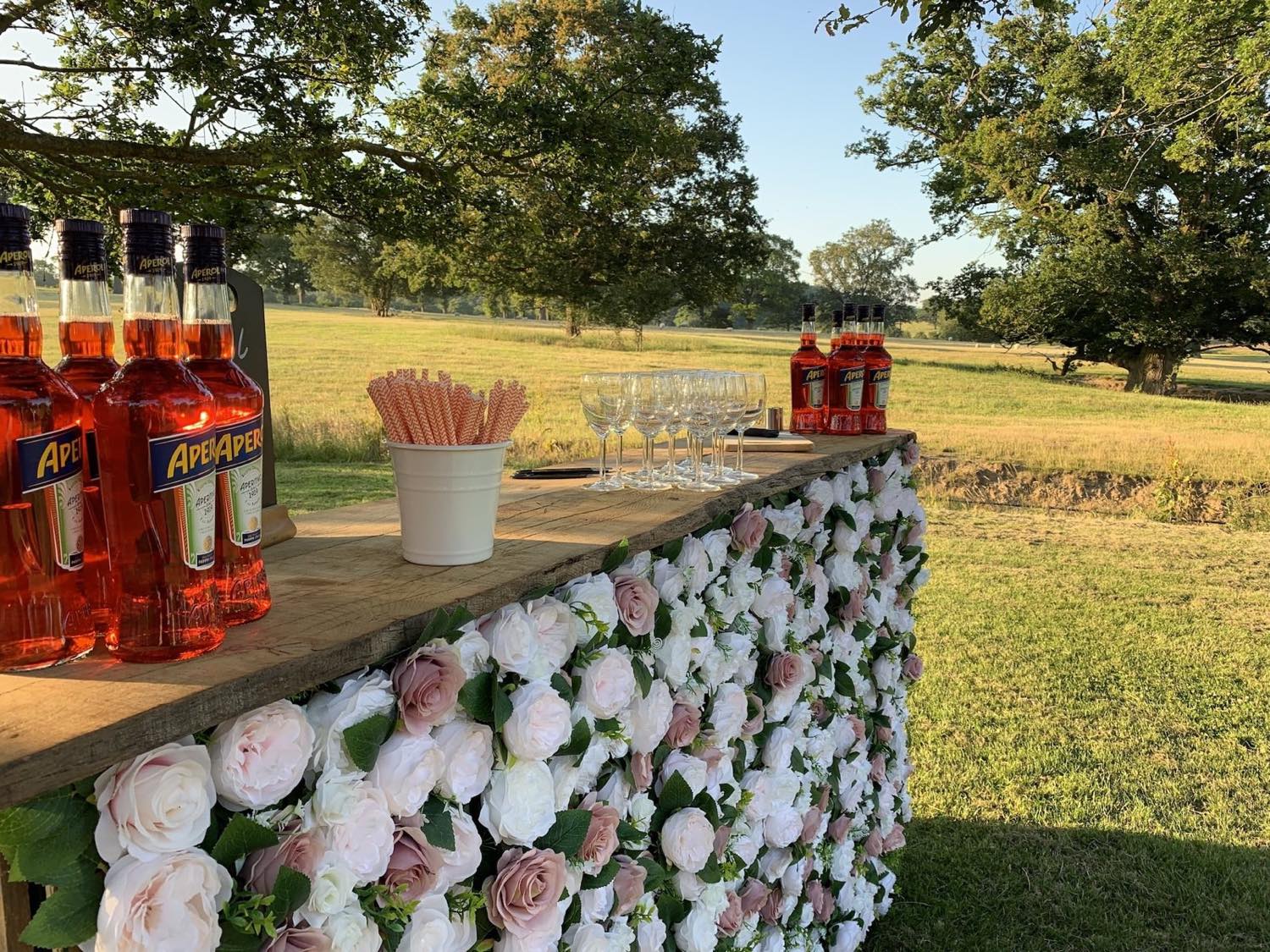 A curved rustic bar dressed with flowers and a full spirits selection inside a function room.